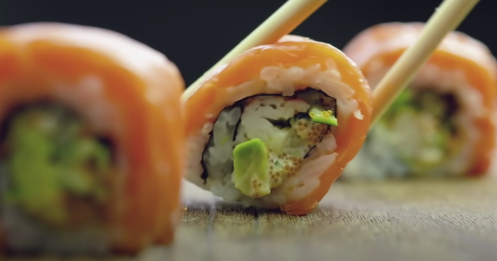 Photo of a maki roll with salmon and wasabi, being picked up using chopsticks
